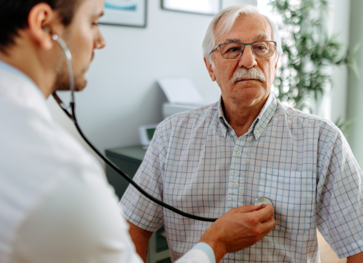 A medical professional in a white coat listening to another person's chest with a stethoscope.