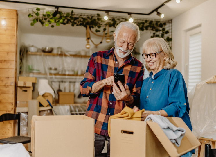 Two people standing indoors, looking at a cellphone, with open cardboard boxes in front of them.