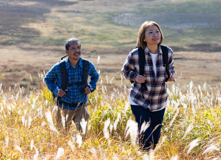 Two people walking through a grassy field on a hillside.